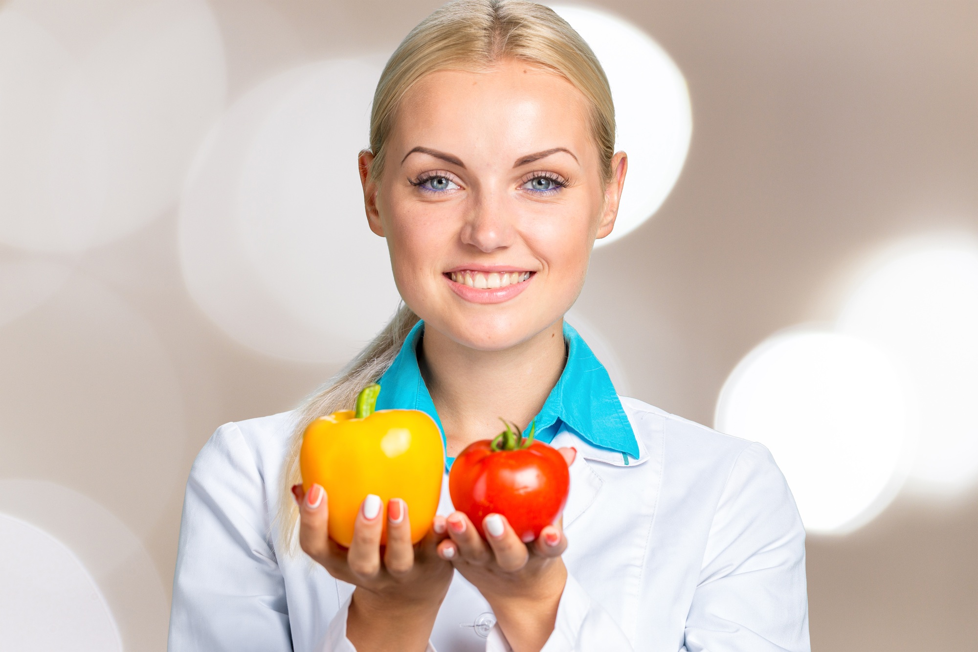Portrait of smiling female doctor in white gown holding fresh vegetables isolated